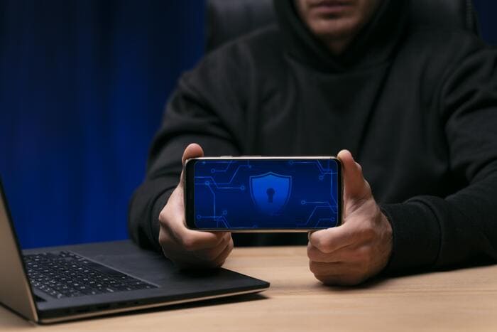 pessoa segurando celular com a tele virada para o leito, na tela uma imagem de fechadura representando a segurança cibernética